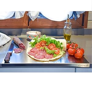 Plan de travail avec dessus tomates, saucisses, couteau coupelle avec fromage, huile et piadine farcite.