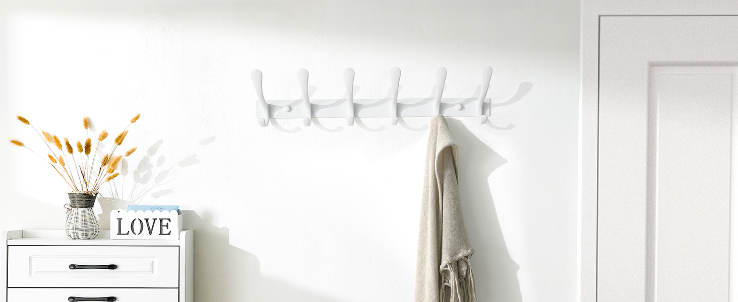 Sur le porche, un porte-manteau mural accroche une écharpe beige à côté d’une commode